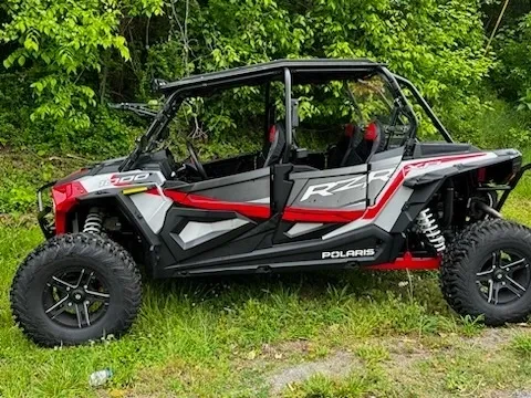 A red and black four-seat polaris rzr parked in the grass.