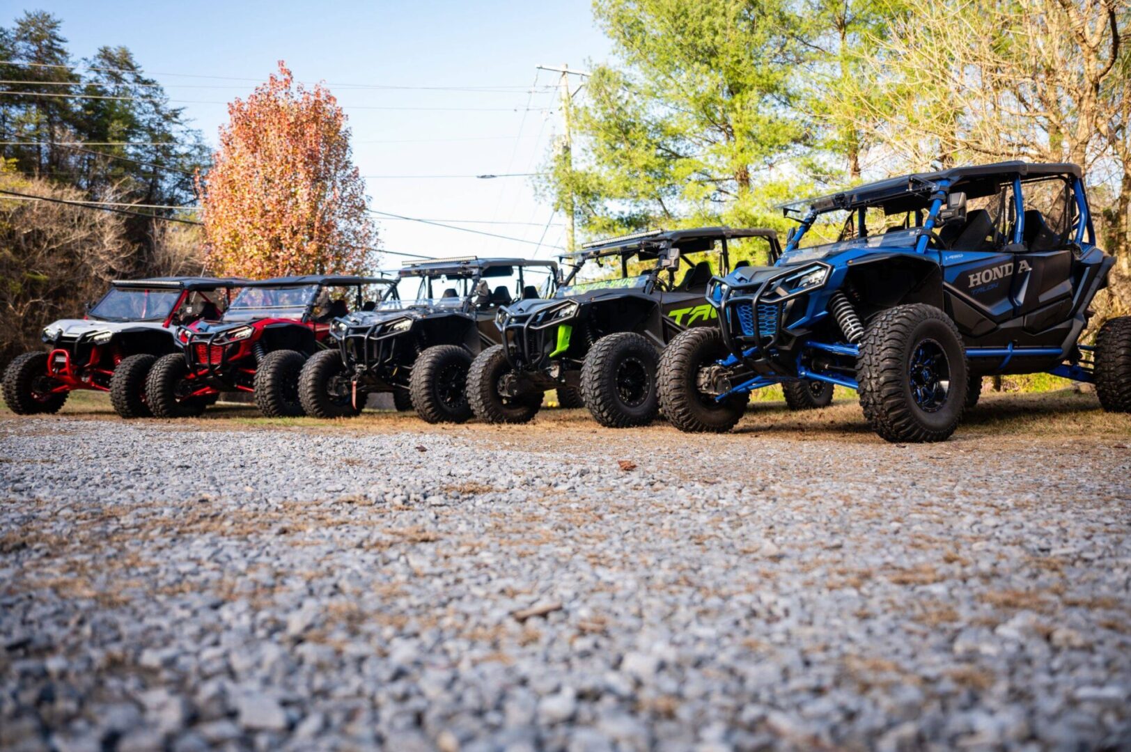 A line of off road vehicles parked on the side of a gravel road.